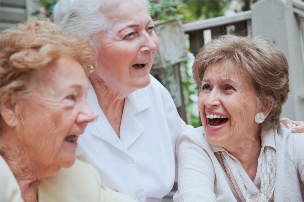 Close up of group of senior women (80s) sitting on steps on front porch of house, laughing.  Focus on woman on right.