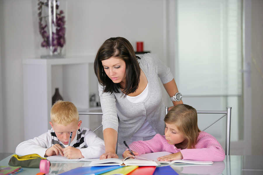 Portrait of young woman helping a boy and a girl in doing homework